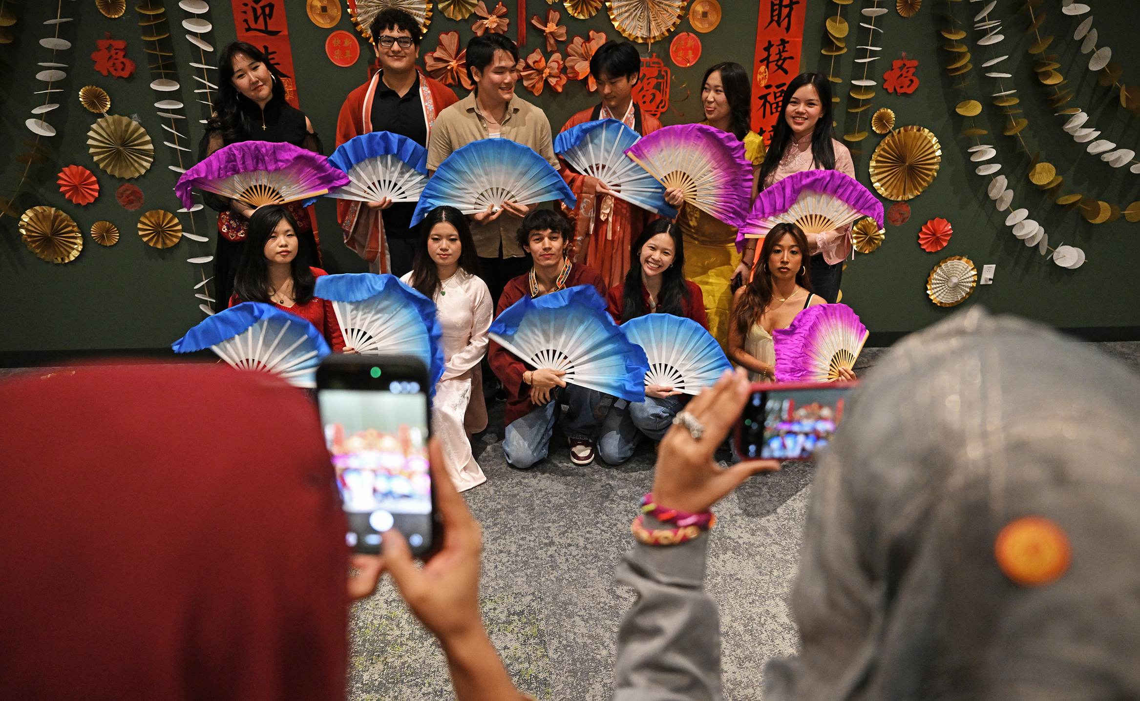 Students in Asian ethic clothing and large colorful fans pose for a group photo.