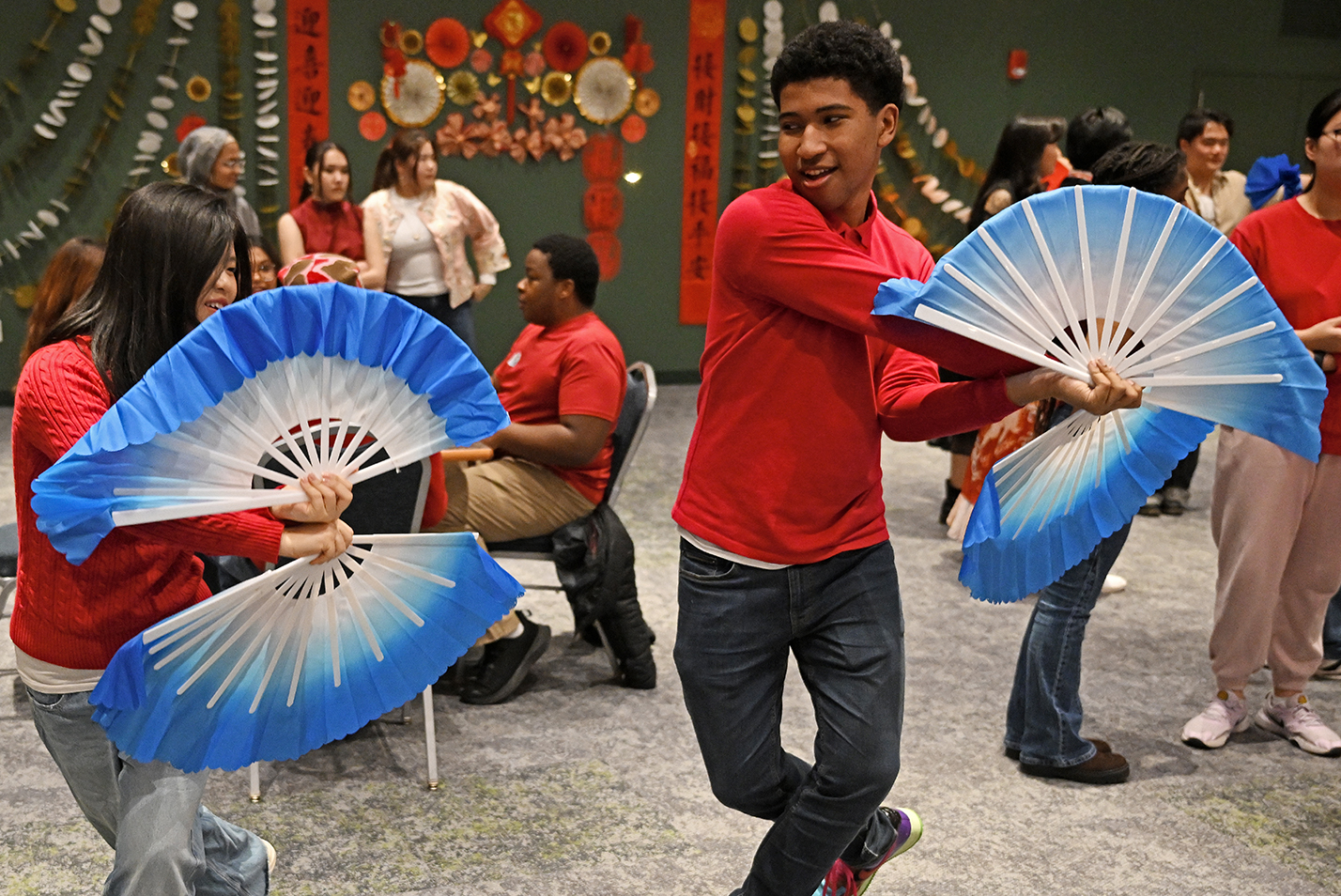 Two college students practice dancing with large hand fans in a ballroom.