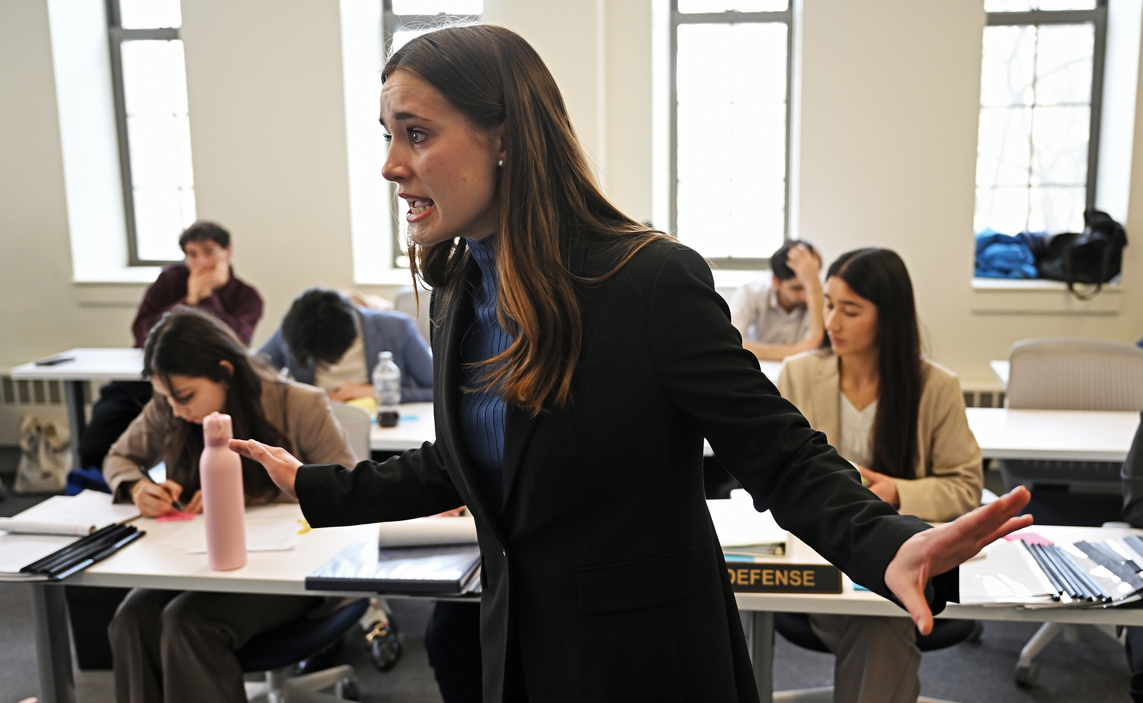 A female student in a suit gestures as she makes a point in a mock trial courtroom.