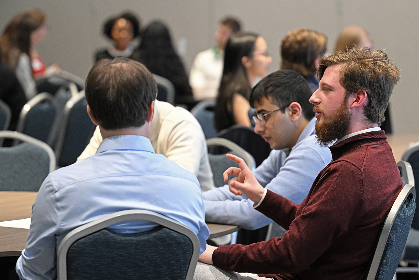 A student in a deep red shirt gestures as he speaks to a table of students.