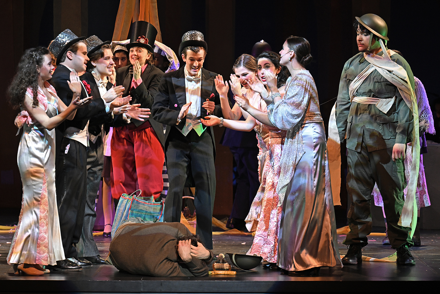 The cast of a musical theater production gather around one actor prone on stage during a performance.