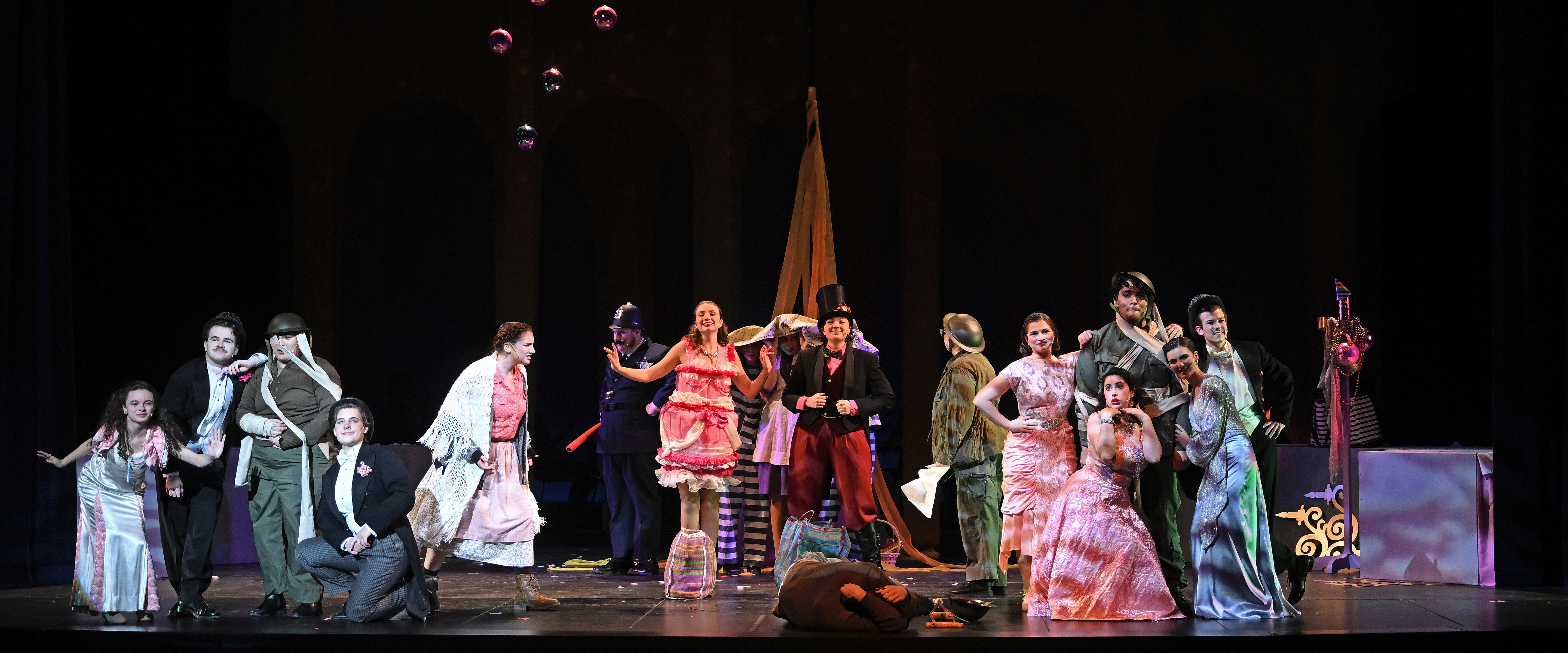 Student actors in colorful costumes perform a musical theater number on stage.