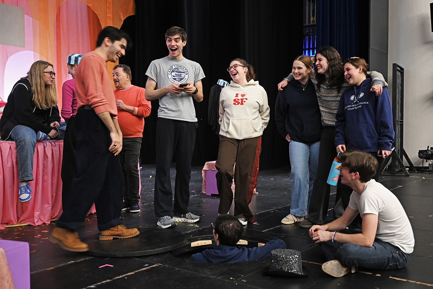 Student actors gather around another climbing out of a trapdoor in the stage while gathering before rehearsal.