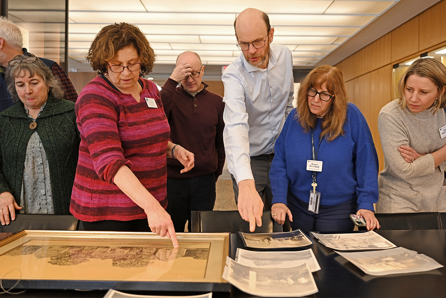 One person points as a group gathers by a table to look at archival photos on display.