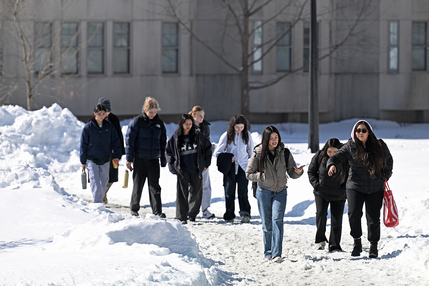 College students in winter coats walk along a snow pathway following a blizzard.