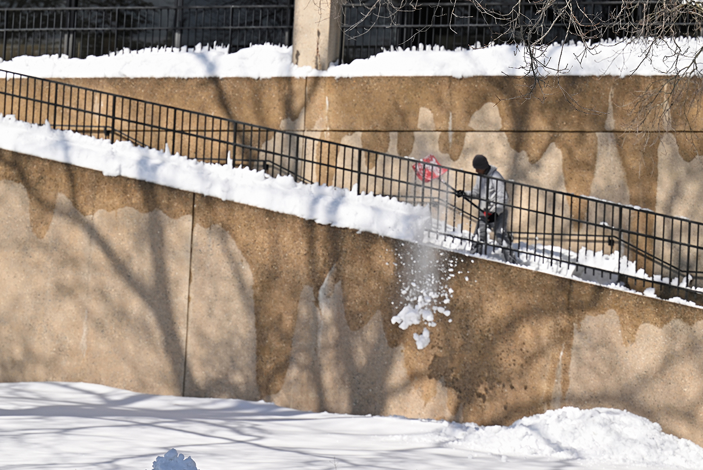A worker throws snow off an outdoor staircase.