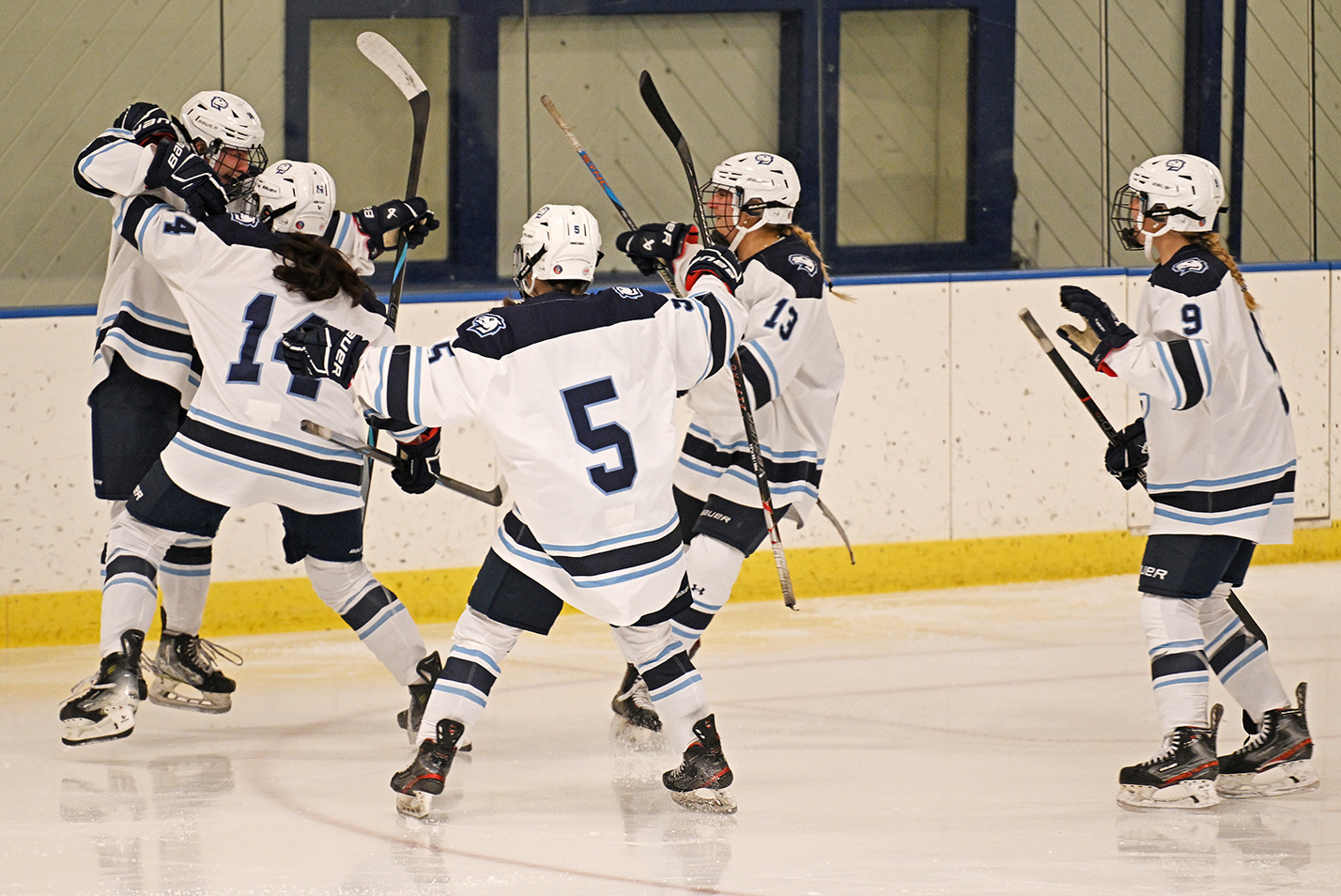 A group of women's ice hockey players race to celebrate a goal.