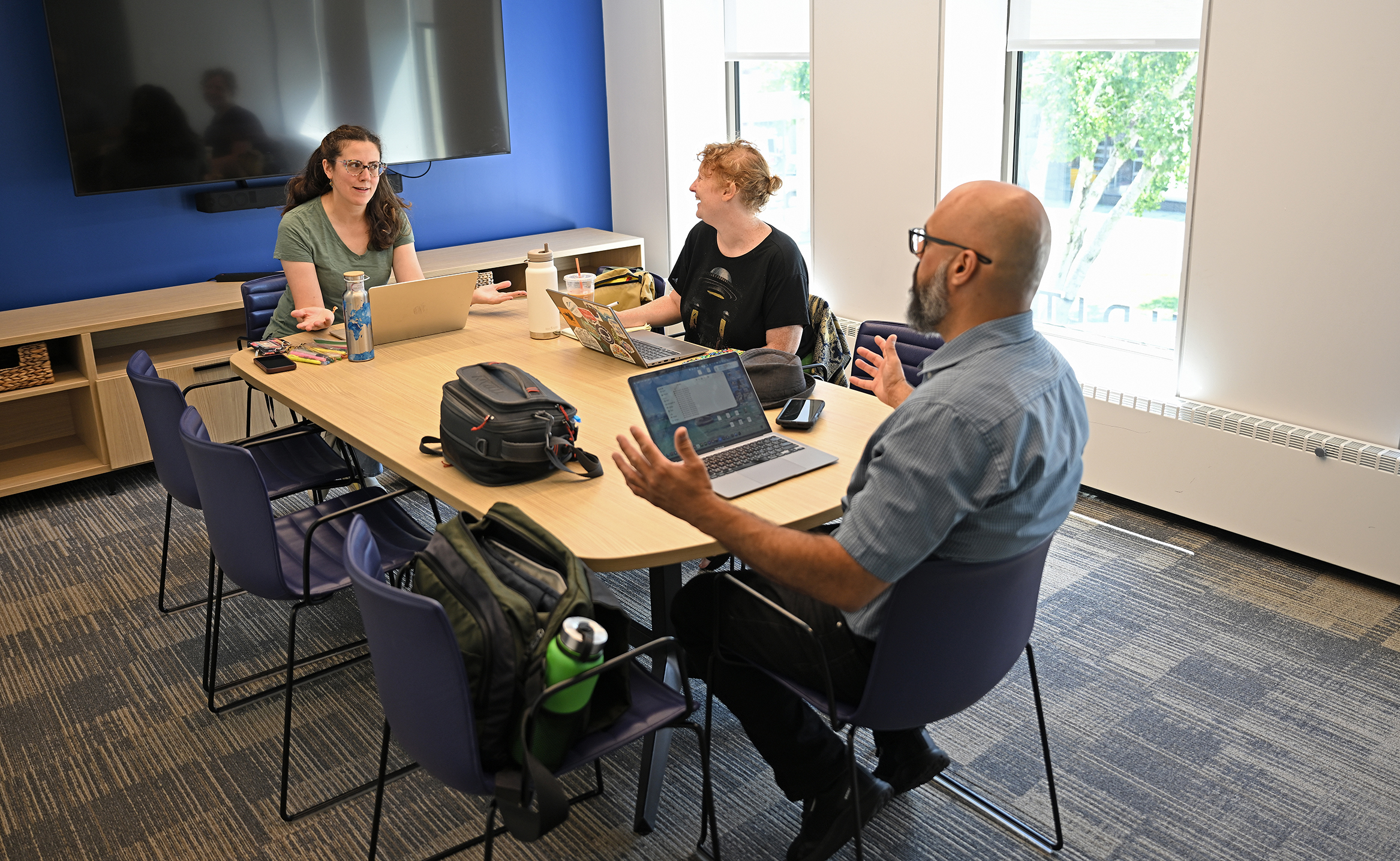 Three college staffers gather around a table with their laptop computers in a small conference room.
