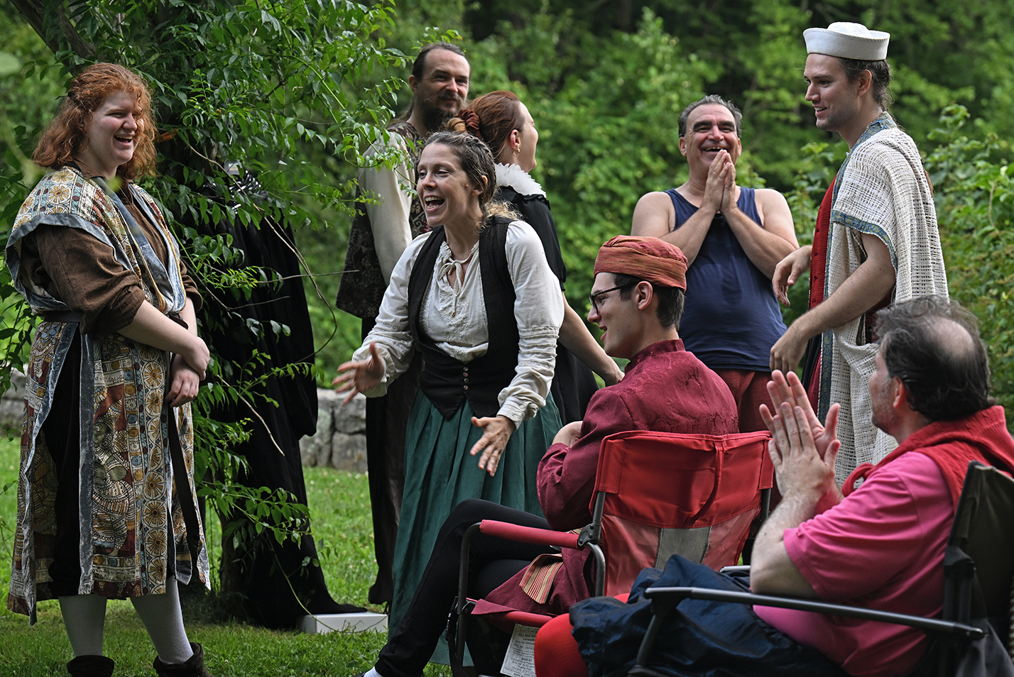 The cast of a theater company in various period garb gather backstage of an outdoor amphitheater before performing Shakespeare's 