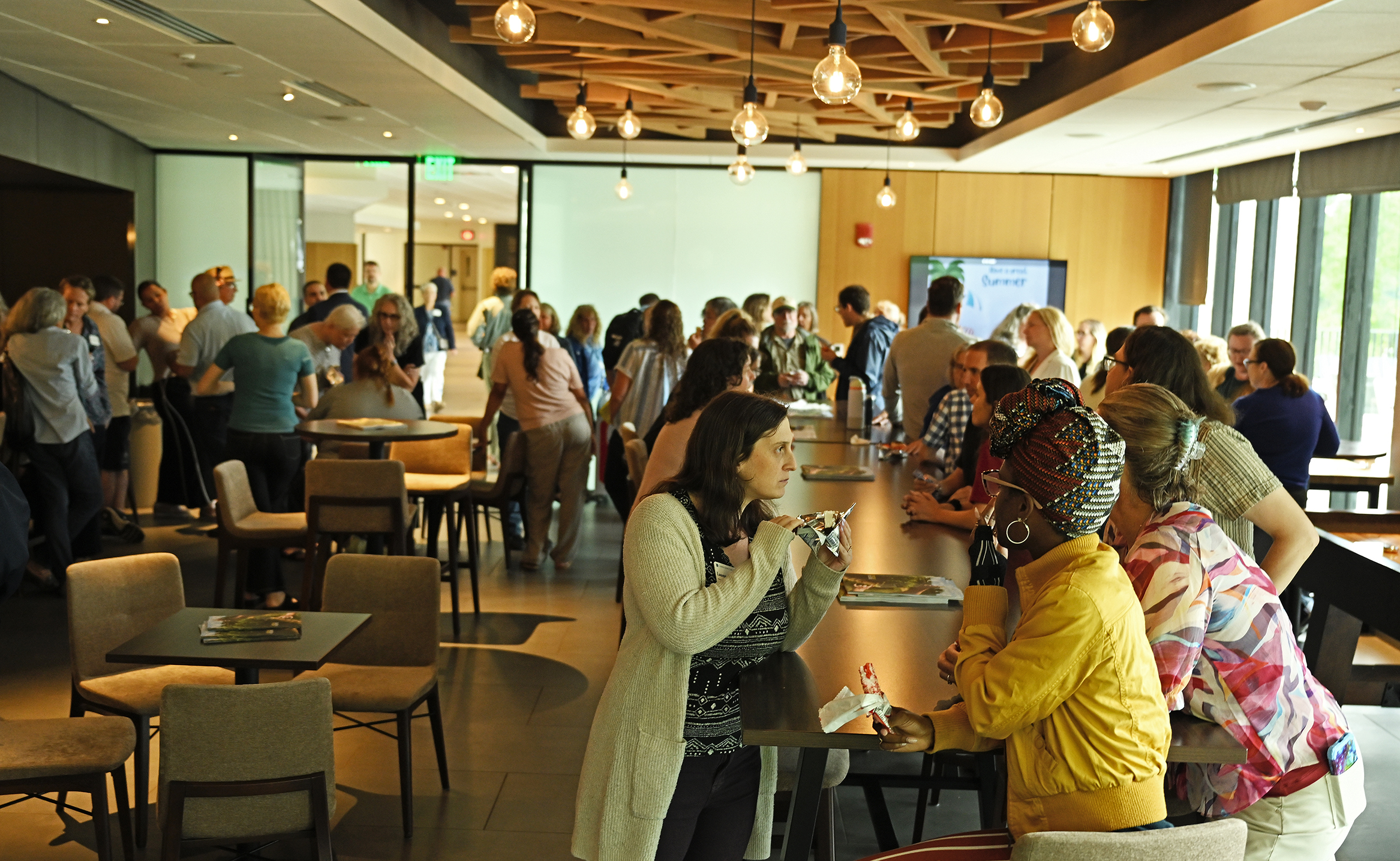 A crowd of college faculty, staff, and students, gather in a campus pub setting eating ice cream and socializing.