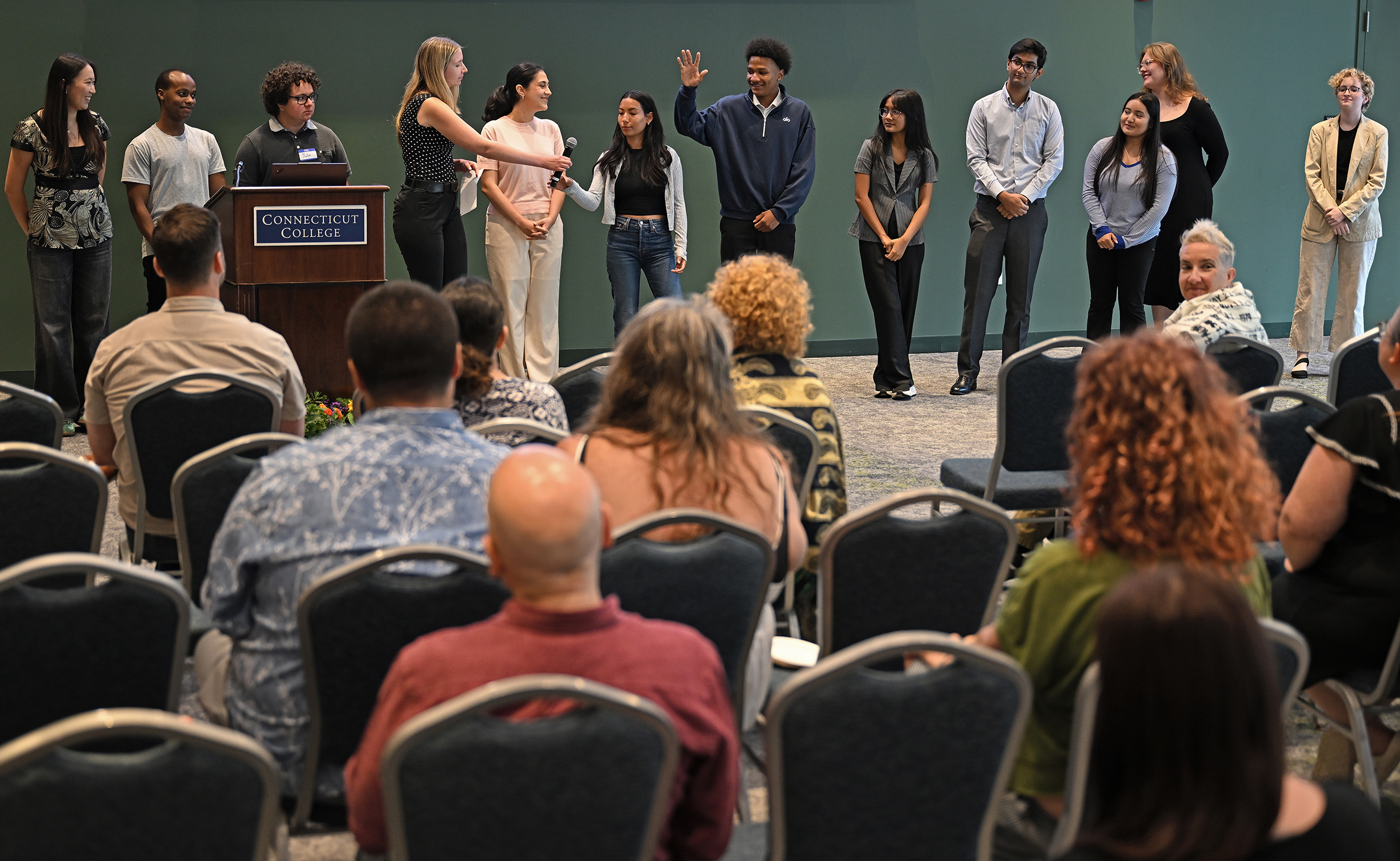 A group of college students stand in front of an audience for a question and answer period after making presentations.