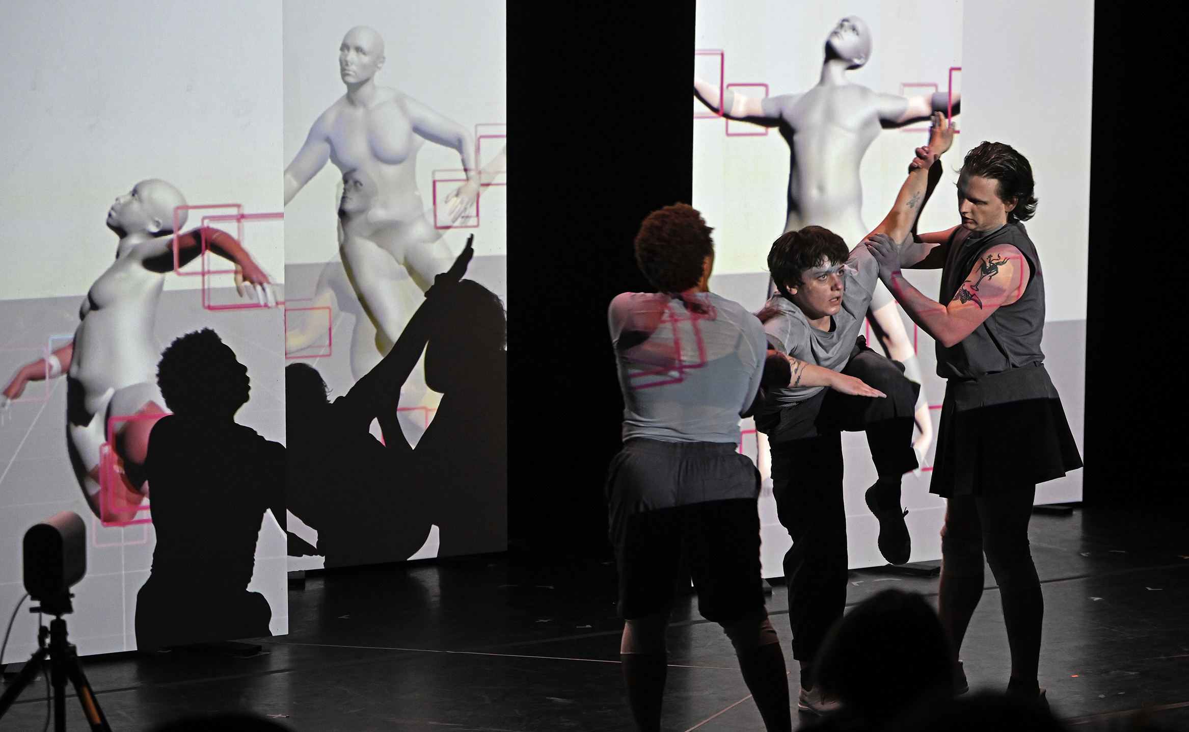 Modern dancers perform an interactive dance in front of video displays of motion capture figures showing their moves in a black box theater space.