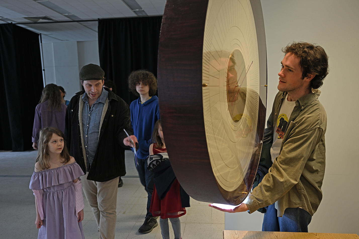 Visitors to an art gallery view a giant clock hanging from the ceiling.