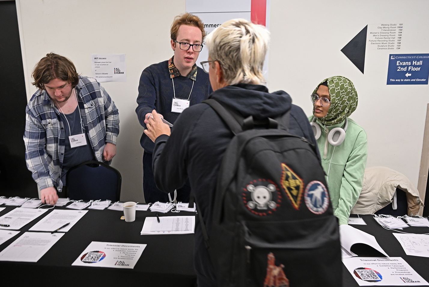 Three student workers hand out registration materials to people arriving at a conference.