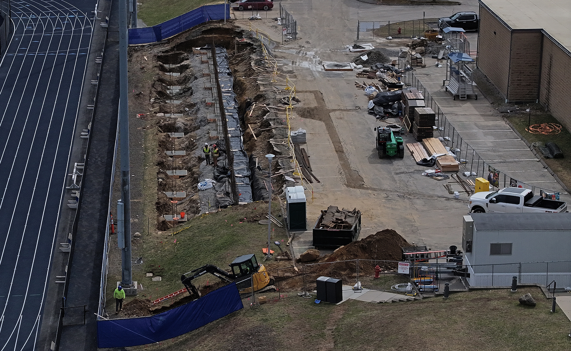 Construction workers build bleachers into an embankment alongside a running track on a college campus.