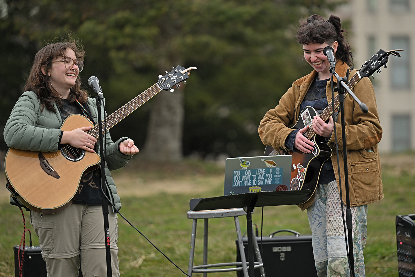 Two student musicians with acoustic guitars laugh together as the perform outdoors.