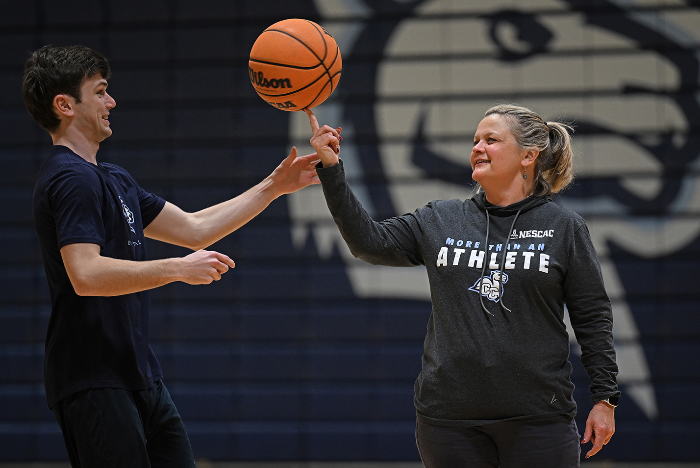 A college basketball player helps his college president to spin a basketball on her finger.