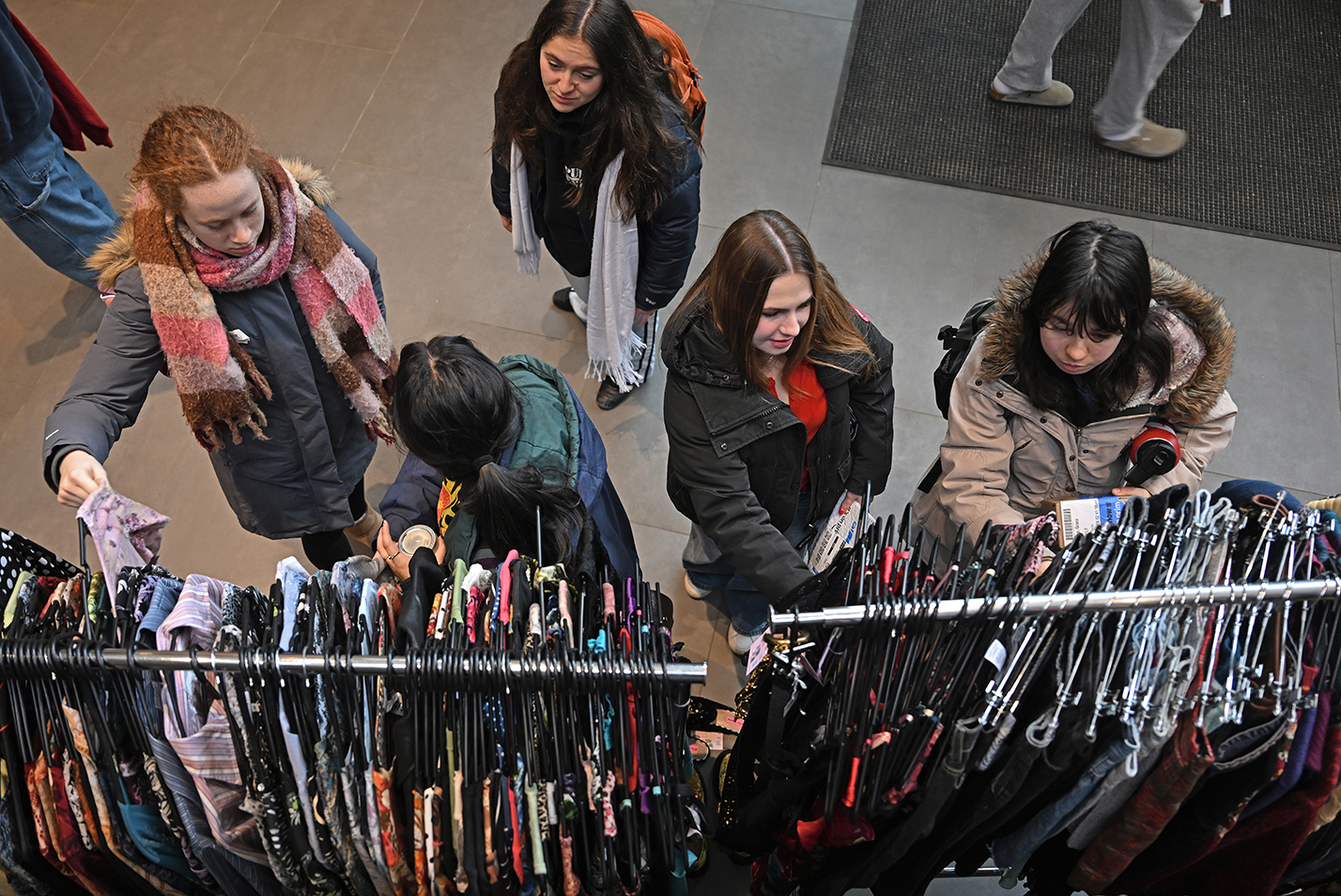 College students seen from overhead look through racks of thrift clothing.