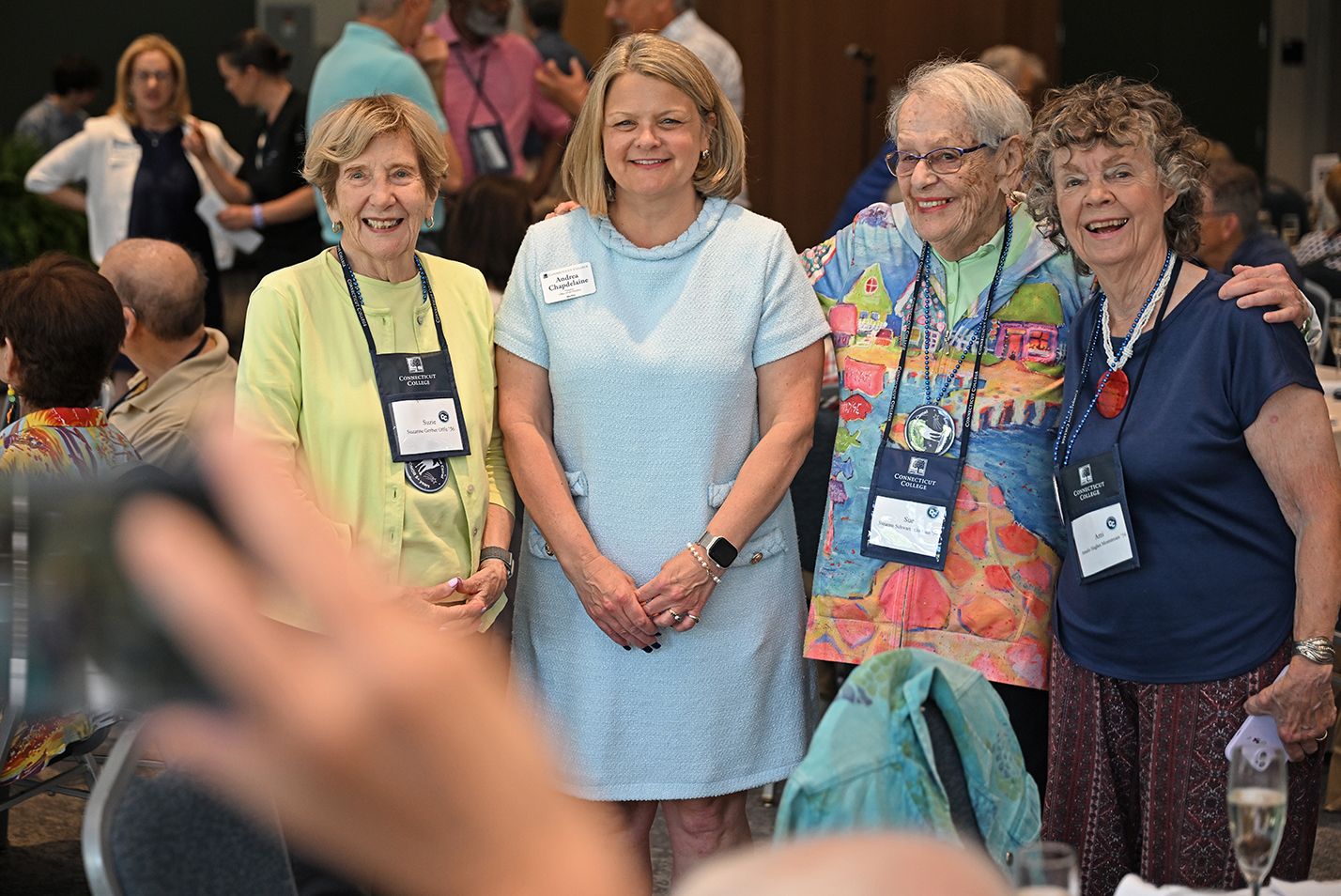 Three older college alumni pose for a photo with the college president in a light blue dress.