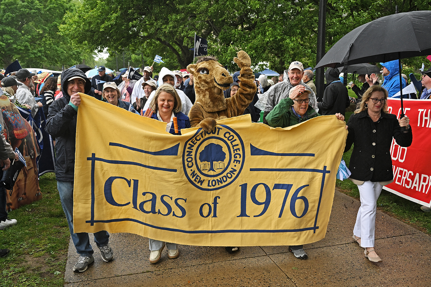 A group of 1976 alumni gather behind a banner proclaiming their class year to march in a reunion parade of classes