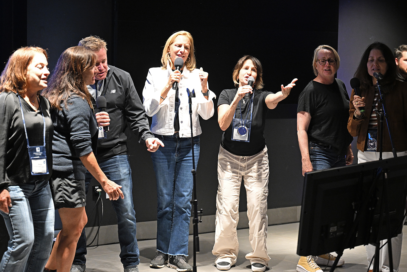 A group of college alumni gather in a line to sing karaoke on a pub stage.