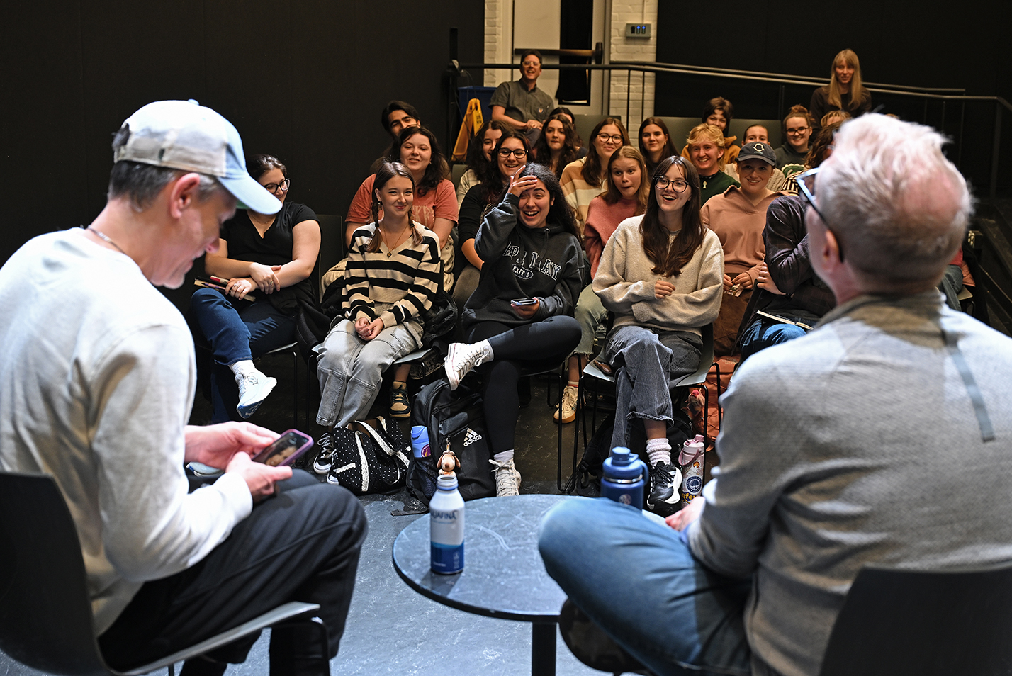 A pair of broadway performers answer questions while seated in front of a small audience of college students in a black box theater space.