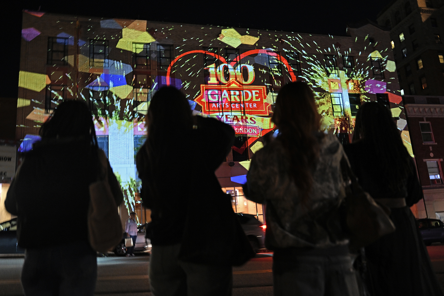 The wall of a theater building is lit up at night with a multimedia projection display featuring virtual fireworks.
