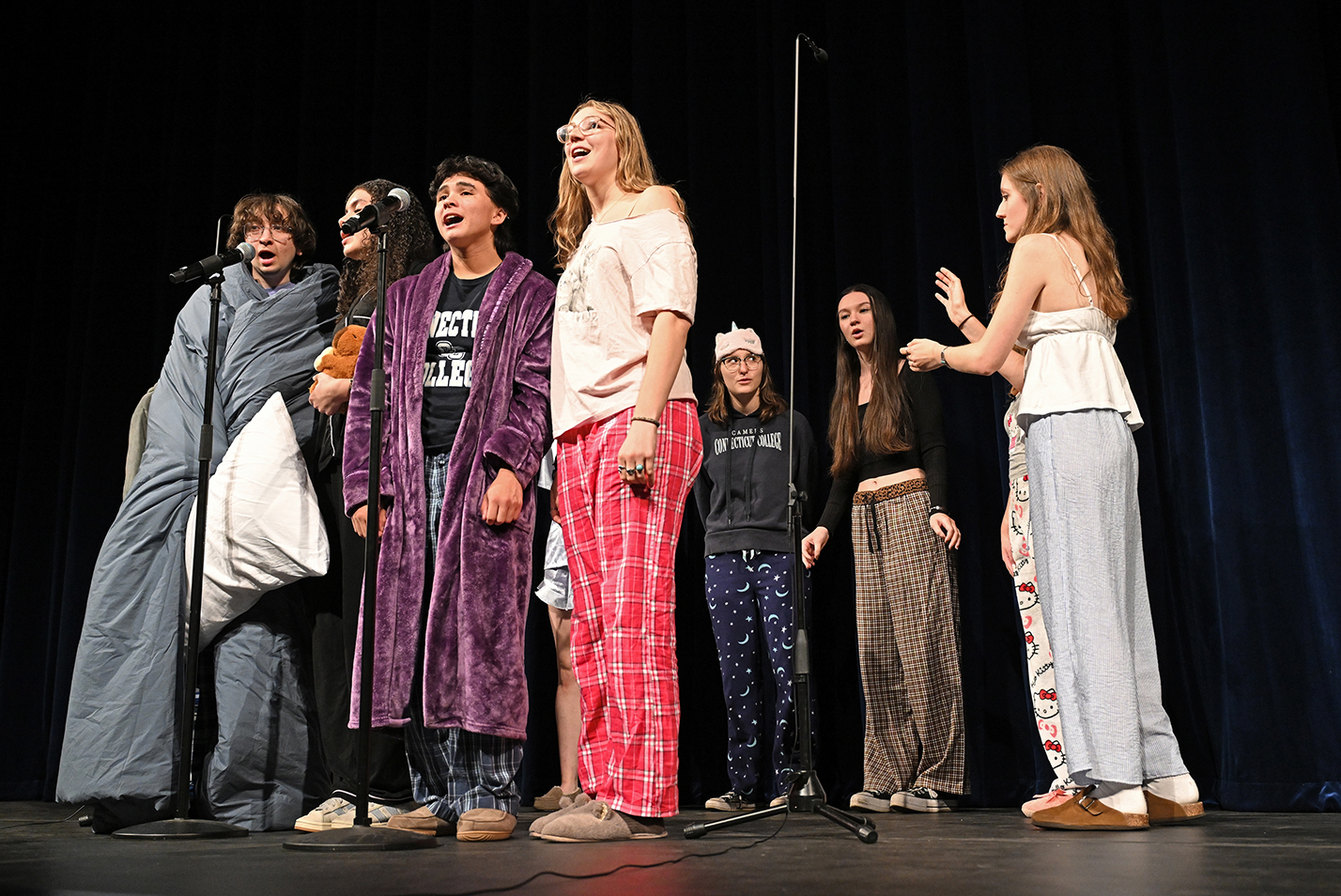 A college a cappelle group wearing pajamas and sleepwear perform on a stage.