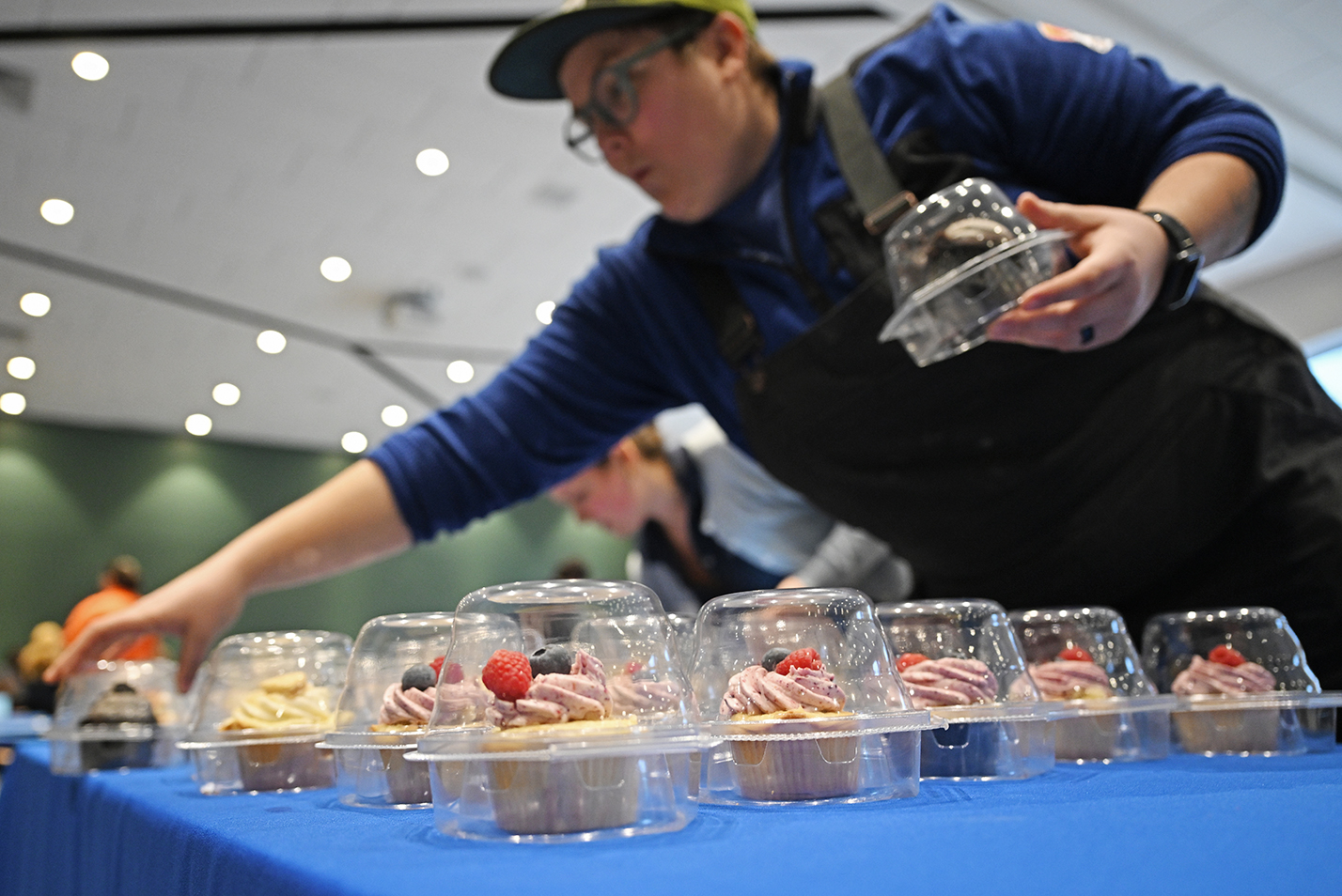 A college student life staffer places cupcakes in clear plastic containers onto a table.
