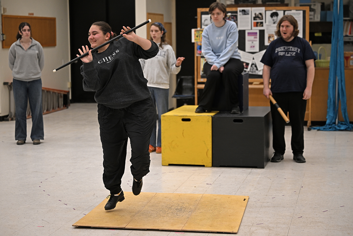 A student actor performs a tap dance as other actors look on during a musical theater rehearsal.