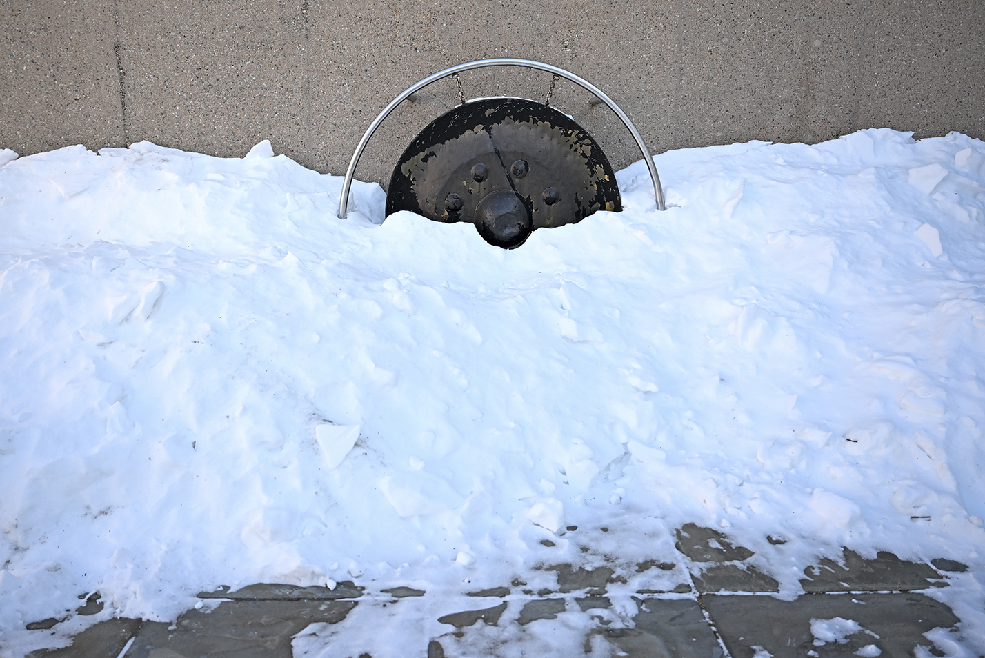A large metal gong stands covered in snow.