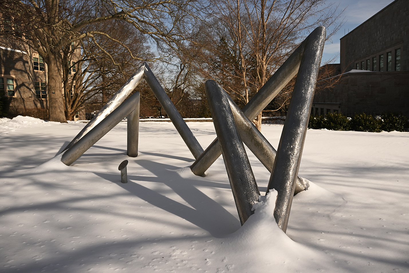 A modern art sculpture crafted of interlocking stainless steel tubes pokes out of a heavy blanket of snow.