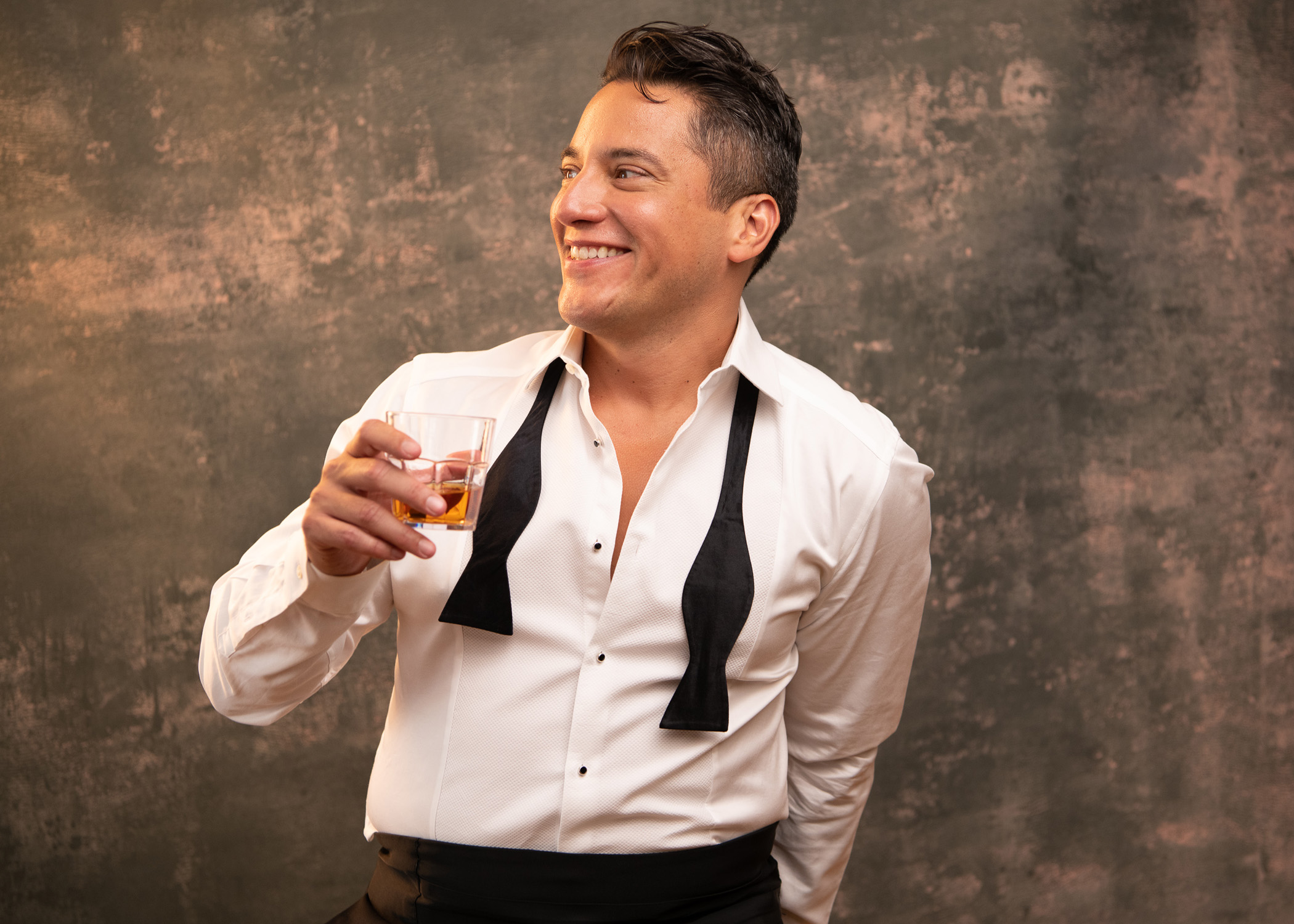 photo of Nicholas Rodriguez in a white shirt and undone bowtie holding a cocktail glass